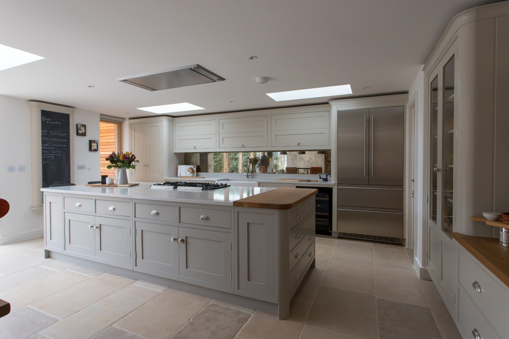 Expansive traditional u-shaped eat-in kitchen in Hertfordshire with a farmhouse sink, shaker cabinets, grey cabinets, quartzite benchtops, metallic splashback, mirror splashback, stainless steel appliances, limestone floors, with island, beige floor and yellow benchtop.