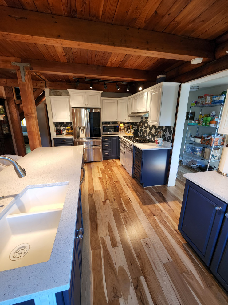 Mid-sized french country l-shaped light wood floor and exposed beam eat-in kitchen photo in Seattle with a single-bowl sink, raised-panel cabinets, white cabinets, solid surface countertops, blue backsplash, ceramic backsplash, stainless steel appliances, an island and white countertops
