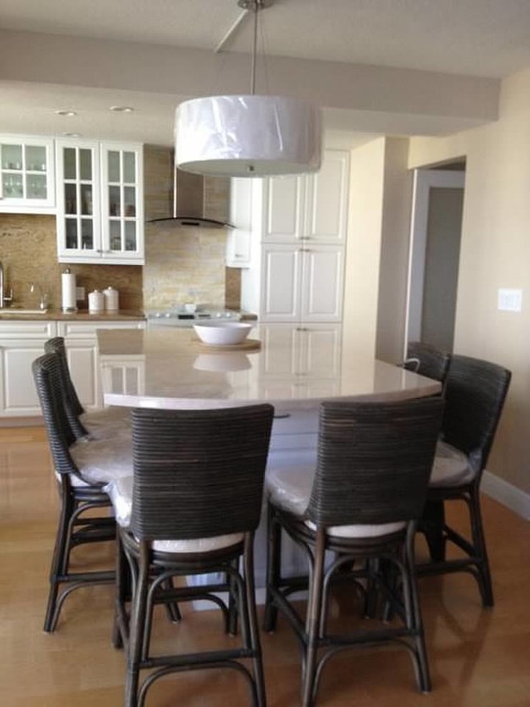 Example of a transitional light wood floor kitchen design with recessed-panel cabinets, white cabinets, quartz countertops, stone tile backsplash, white appliances and an island