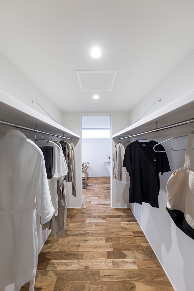 Photo of a modern gender neutral walk-in wardrobe in Other with open cabinets, white cabinets, medium hardwood flooring, brown floors and a wallpapered ceiling.