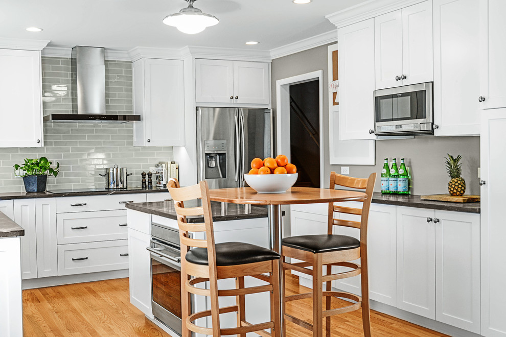 Inspiration for a mid-sized transitional u-shaped medium tone wood floor eat-in kitchen remodel with shaker cabinets, white cabinets, onyx countertops, gray backsplash, subway tile backsplash, stainless steel appliances, an island and a farmhouse sink