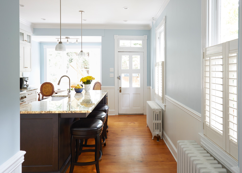 Transitional medium tone wood floor eat-in kitchen photo in DC Metro with a farmhouse sink, recessed-panel cabinets, white cabinets, granite countertops, white backsplash, subway tile backsplash, stainless steel appliances and an island