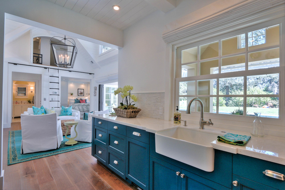 Small beach style u-shaped separate kitchen in San Francisco with a farmhouse sink, glass-front cabinets, blue cabinets, white splashback, matchstick tile splashback, stainless steel appliances and medium hardwood floors.