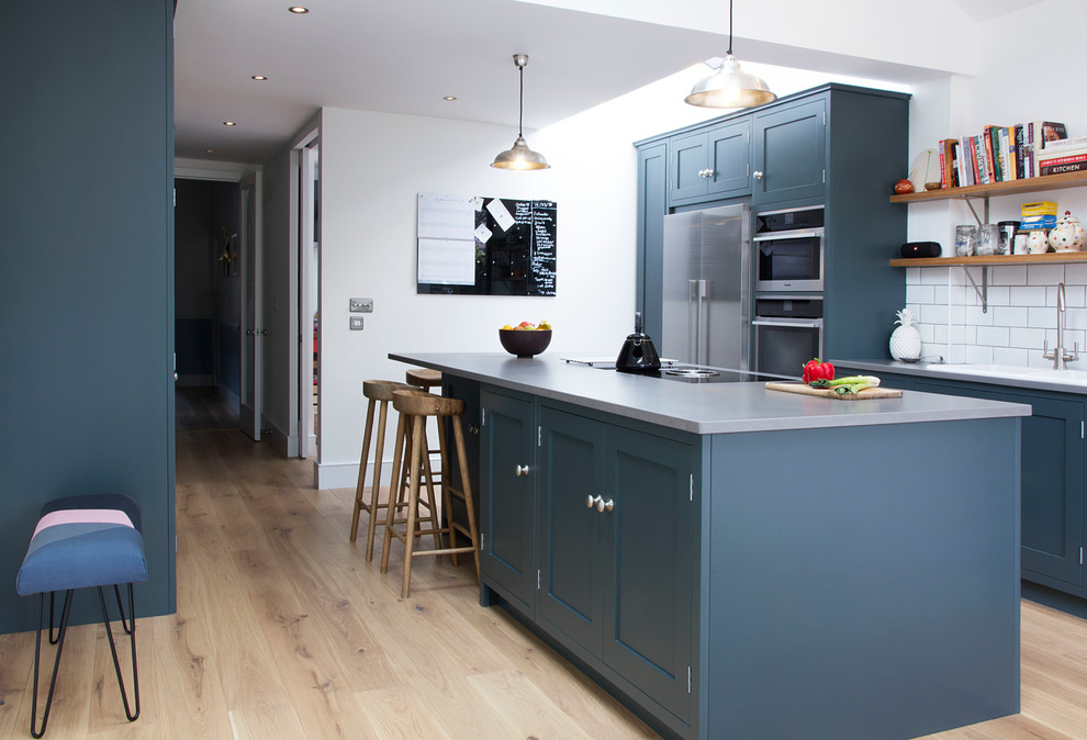 Design ideas for a small contemporary single-wall kitchen in London with recessed-panel cabinets, blue cabinets, concrete benchtops, white splashback, subway tile splashback, stainless steel appliances, light hardwood floors, with island, beige floor and grey benchtop.