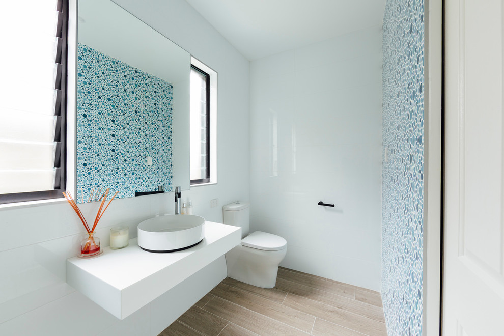 Inspiration for a small contemporary bathroom in Sydney with a two-piece toilet, multi-coloured tile, porcelain tile, white walls, light hardwood floors, a vessel sink and solid surface benchtops.