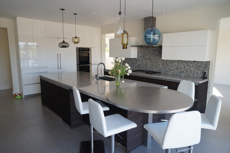 Design ideas for a large eclectic l-shaped open plan kitchen in Orange County with a double-bowl sink, flat-panel cabinets, white cabinets, glass benchtops, black splashback, glass tile splashback, stainless steel appliances, porcelain floors and with island.