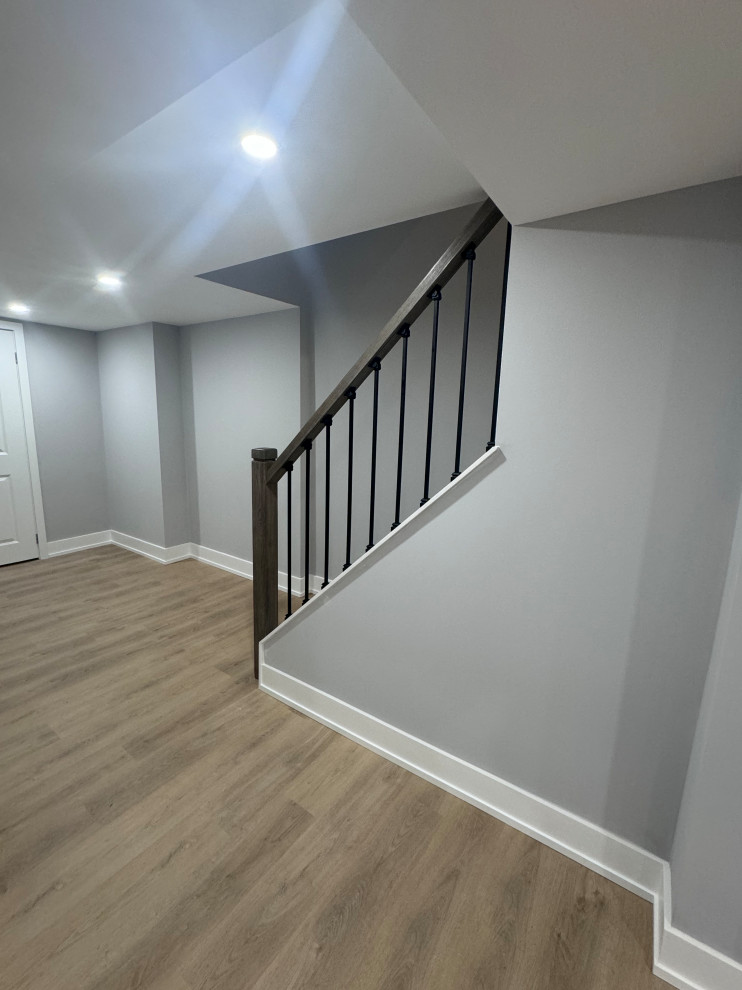 Photo of a medium sized modern basement in Toronto with a home bar, grey walls, laminate floors, a standard fireplace, a stone fireplace surround and beige floors.