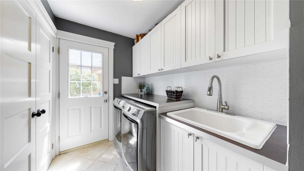 Photo of a small country galley dedicated laundry room in Philadelphia with a drop-in sink, beaded inset cabinets, white cabinets, wood benchtops, white splashback, glass tile splashback, grey walls, terra-cotta floors, a side-by-side washer and dryer, white floor and multi-coloured benchtop.