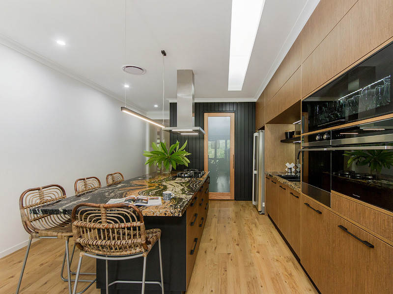 Contemporary kitchen in Brisbane with an undermount sink, medium wood cabinets, granite benchtops, mirror splashback, black appliances, vinyl floors and with island.