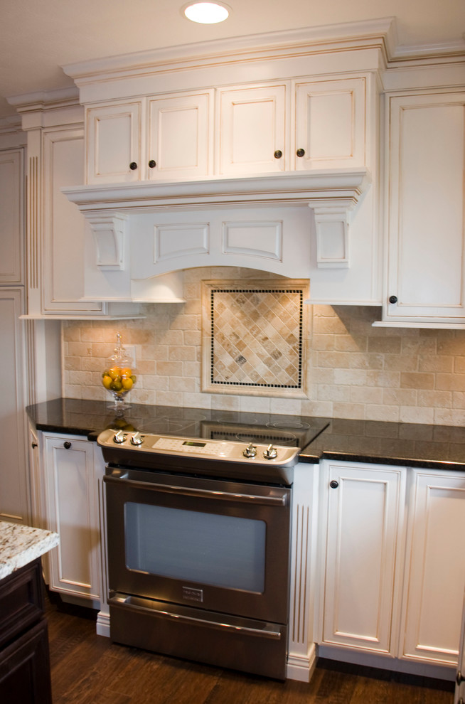 Inspiration for a large transitional u-shaped medium tone wood floor kitchen remodel in Cincinnati with an undermount sink, recessed-panel cabinets, white cabinets, granite countertops, beige backsplash, stone tile backsplash, stainless steel appliances and an island