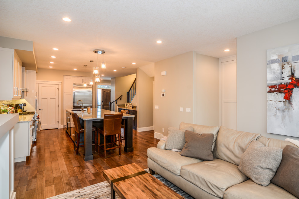 Example of a large transitional l-shaped medium tone wood floor open concept kitchen design in Calgary with an undermount sink, shaker cabinets, white cabinets, granite countertops, gray backsplash, porcelain backsplash, stainless steel appliances and an island