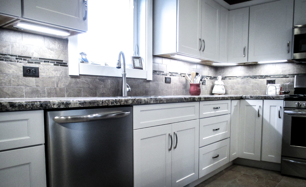 Example of a mid-sized transitional l-shaped vinyl floor eat-in kitchen design with white cabinets, stainless steel appliances, an island, shaker cabinets, granite countertops, gray backsplash and ceramic backsplash