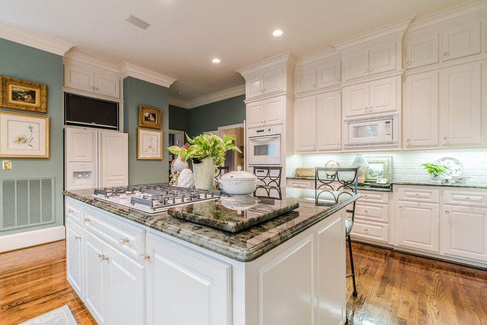 Photo of an expansive traditional open plan kitchen in Dallas with a double-bowl sink, white splashback, subway tile splashback, white appliances, light hardwood floors and with island.
