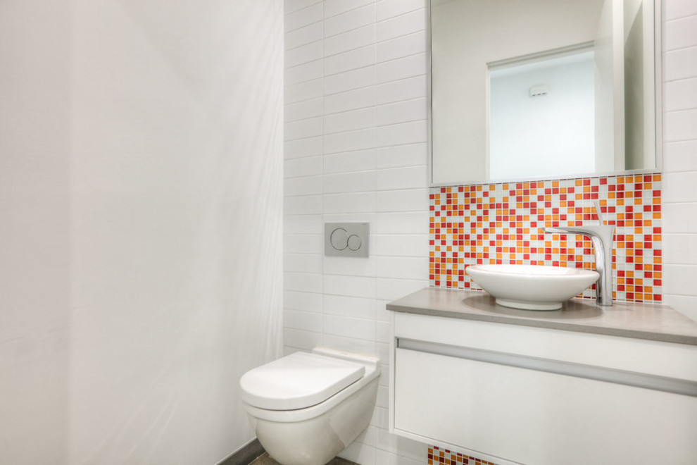 Small modern powder room in Houston with flat-panel cabinets, white cabinets, multi-coloured tile, mosaic tile, white walls, travertine floors, solid surface benchtops, beige floor, a wall-mount toilet and a vessel sink.