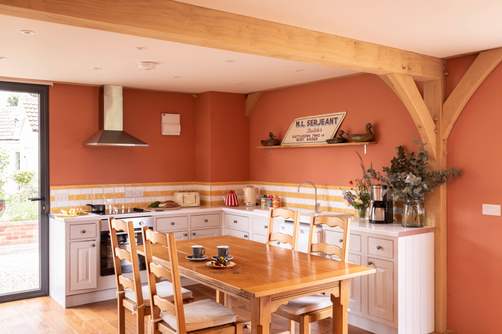 Country l-shaped kitchen/diner with beaded cabinets, grey cabinets, multi-coloured splashback, stainless steel appliances, medium hardwood flooring, brown floors and grey worktops.