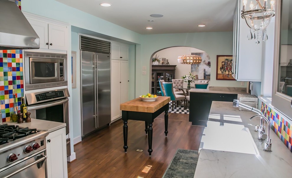 Photo of a large transitional galley eat-in kitchen in Dallas with a farmhouse sink, white cabinets, multi-coloured splashback, glass tile splashback, stainless steel appliances, medium hardwood floors, marble benchtops, brown floor, recessed-panel cabinets, with island and white benchtop.