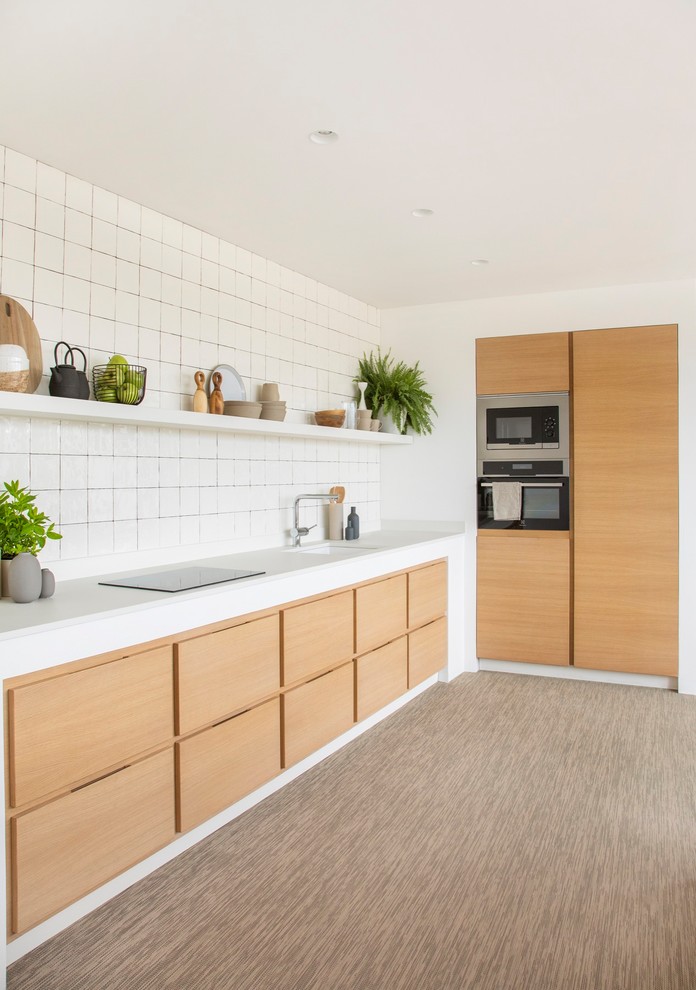 This is an example of a scandinavian l-shaped kitchen in Barcelona with an undermount sink, flat-panel cabinets, light wood cabinets, white splashback, stainless steel appliances, beige floor and white benchtop.