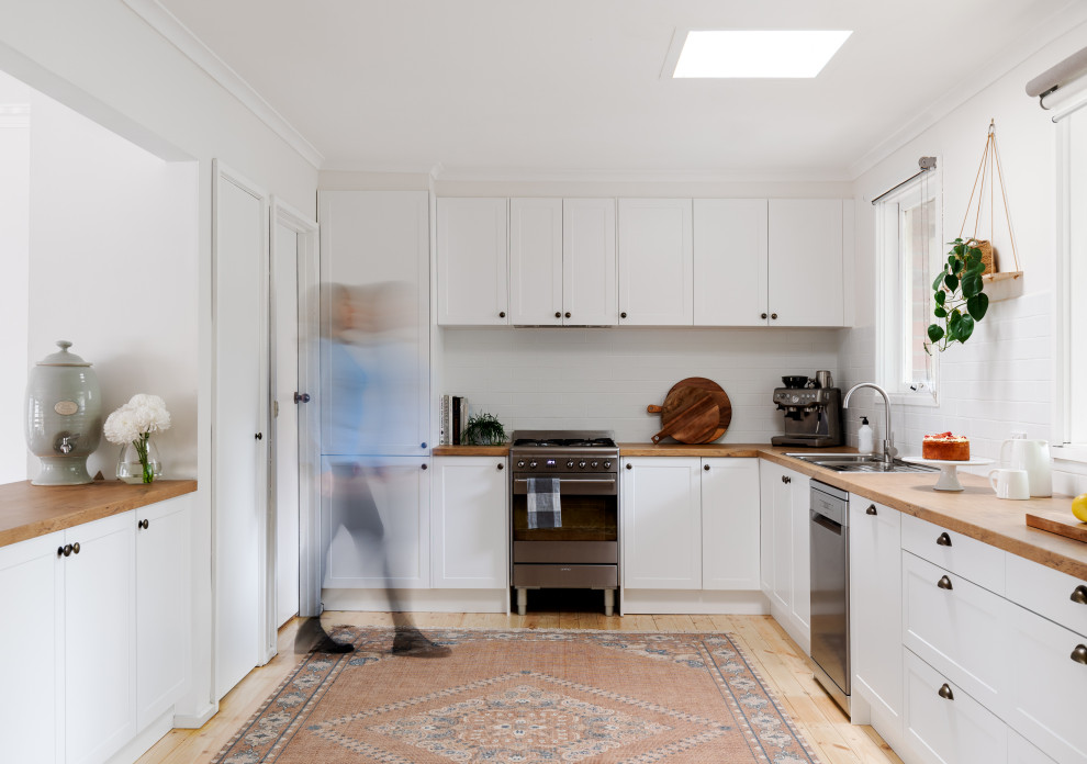 Inspiration for a large contemporary u-shaped kitchen pantry in Melbourne with a drop-in sink, shaker cabinets, white cabinets, laminate benchtops, white splashback, subway tile splashback, stainless steel appliances and light hardwood floors.