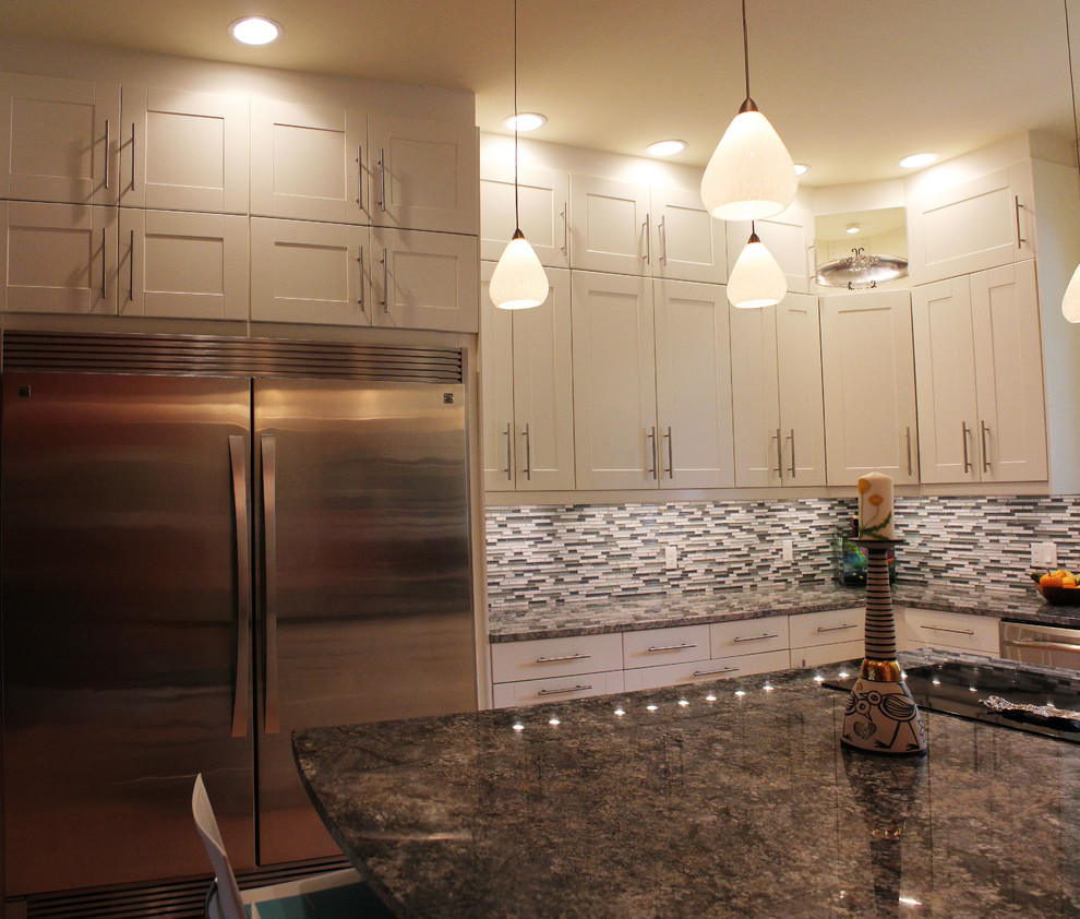 Example of a large trendy u-shaped light wood floor eat-in kitchen design with an undermount sink, shaker cabinets, white cabinets, granite countertops, multicolored backsplash, glass tile backsplash, stainless steel appliances and an island