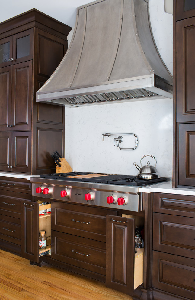 Example of a large transitional l-shaped light wood floor open concept kitchen design in Atlanta with a farmhouse sink, raised-panel cabinets, dark wood cabinets, quartz countertops, white backsplash, stone slab backsplash, stainless steel appliances and an island