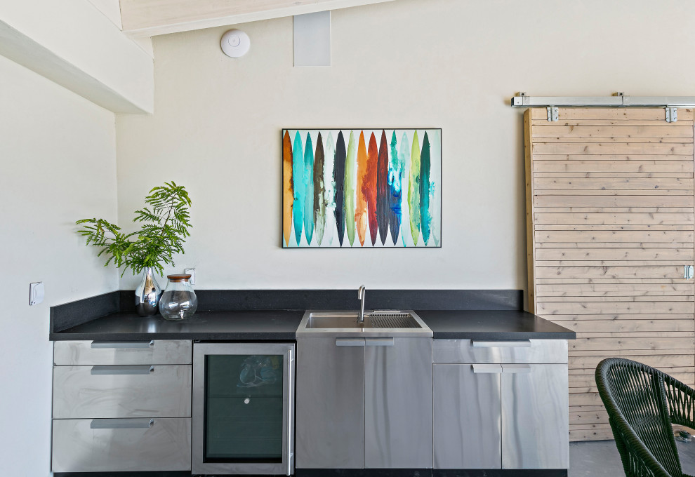 Inspiration for a small contemporary galley open plan kitchen in San Francisco with an integrated sink, flat-panel cabinets, stainless steel cabinets, quartz benchtops, black splashback, engineered quartz splashback, stainless steel appliances, concrete floors, no island, grey floor, black benchtop and exposed beam.