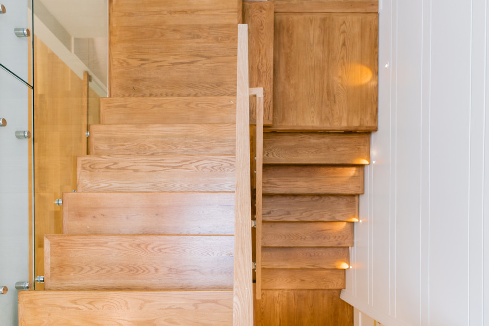 Inspiration for a transitional wood u-shaped staircase in Toronto with wood risers, glass railing and panelled walls.