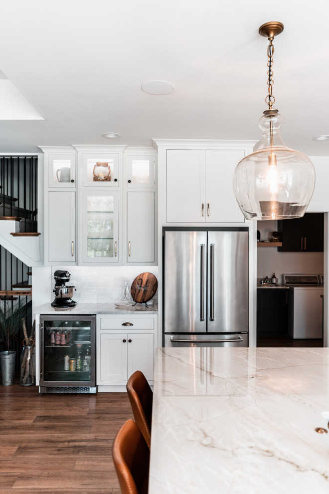 Example of a large transitional l-shaped light wood floor open concept kitchen design with an undermount sink, shaker cabinets, white cabinets, quartzite countertops, multicolored backsplash, porcelain backsplash, stainless steel appliances and an island