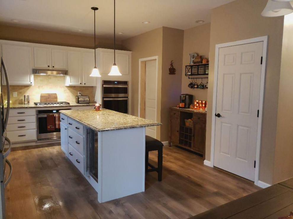 Enclosed kitchen - large l-shaped medium tone wood floor and brown floor enclosed kitchen idea with a farmhouse sink, raised-panel cabinets, white cabinets, granite countertops, beige backsplash, stone tile backsplash, stainless steel appliances, an island and beige countertops