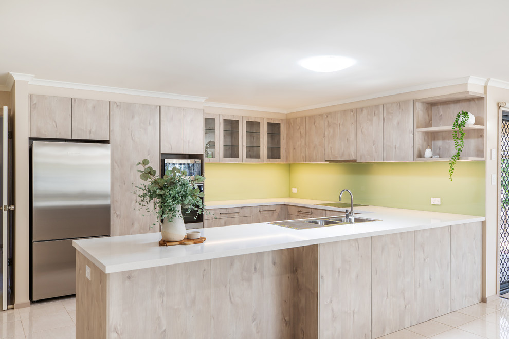 Inspiration for a mid-sized modern u-shaped kitchen pantry in Adelaide with a double-bowl sink, flat-panel cabinets, light wood cabinets, quartz benchtops, green splashback, glass sheet splashback, stainless steel appliances, porcelain floors, a peninsula, white floor and white benchtop.
