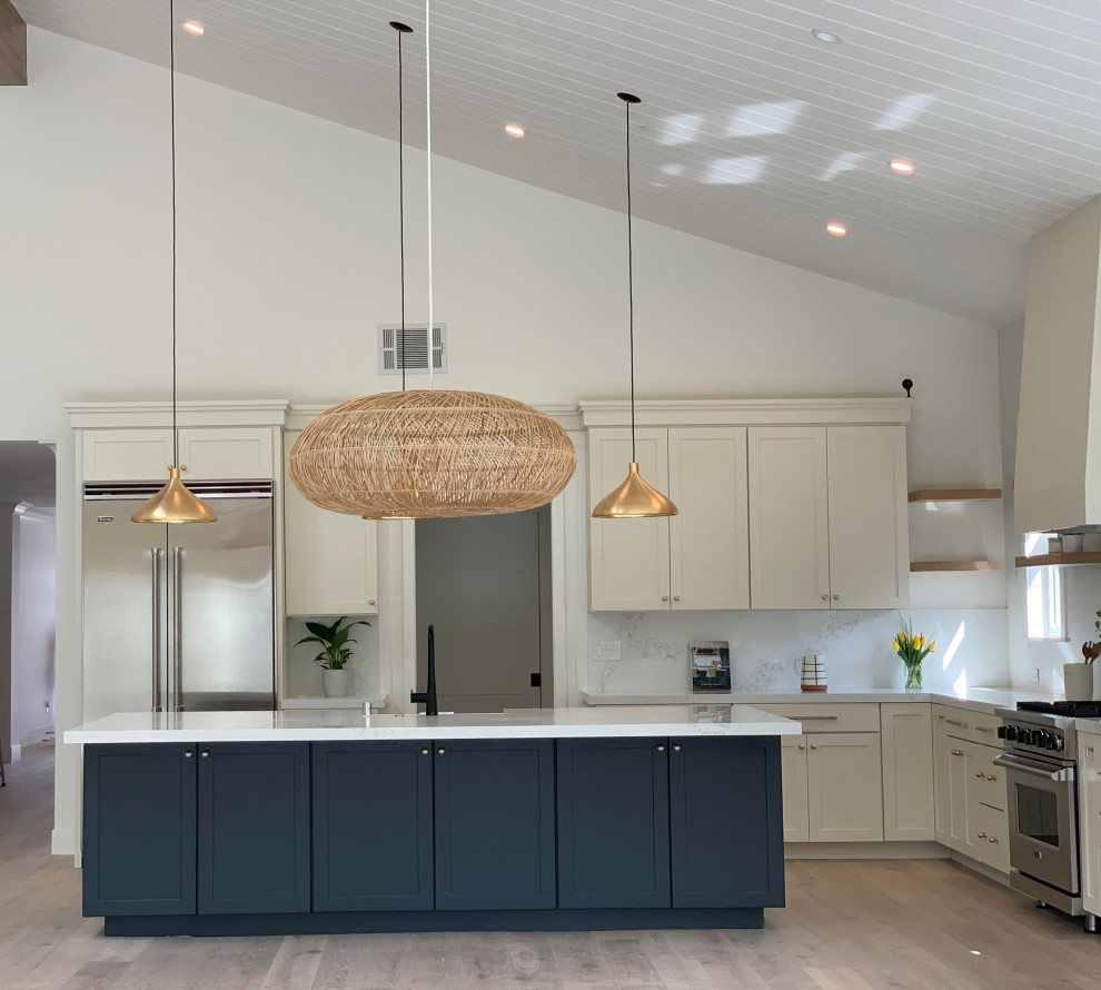 Large country l-shaped open plan kitchen in San Francisco with a farmhouse sink, shaker cabinets, white cabinets, quartz benchtops, white splashback, engineered quartz splashback, stainless steel appliances, light hardwood floors, with island, grey floor, white benchtop and vaulted.