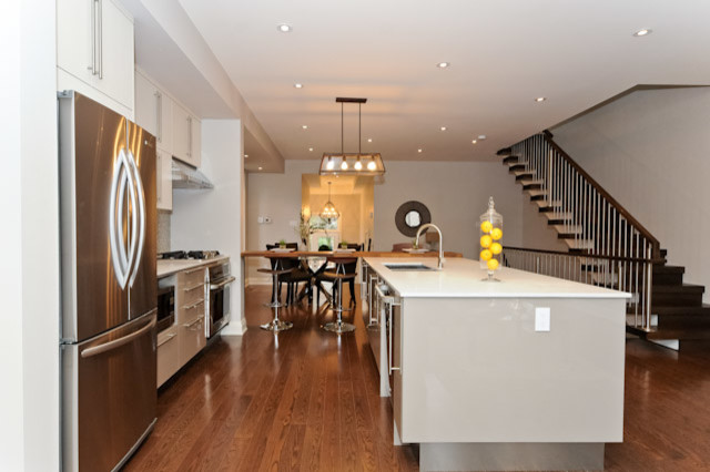 This is an example of a modern l-shaped kitchen in Ottawa with a double-bowl sink, shaker cabinets, white cabinets, quartz benchtops, grey splashback, ceramic splashback, stainless steel appliances and medium hardwood floors.
