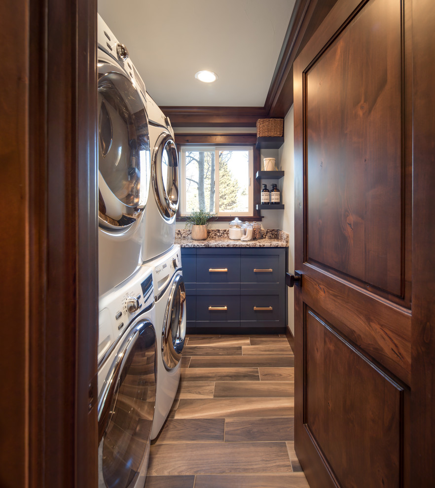 Dedicated laundry room - small transitional medium tone wood floor and brown floor dedicated laundry room idea in Denver with shaker cabinets, blue cabinets, a stacked washer/dryer and multicolored countertops