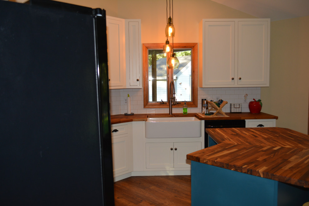 Photo of a small transitional u-shaped eat-in kitchen in Other with a farmhouse sink, recessed-panel cabinets, white cabinets, wood benchtops, white splashback, ceramic splashback, black appliances, medium hardwood floors, with island, brown floor and brown benchtop.