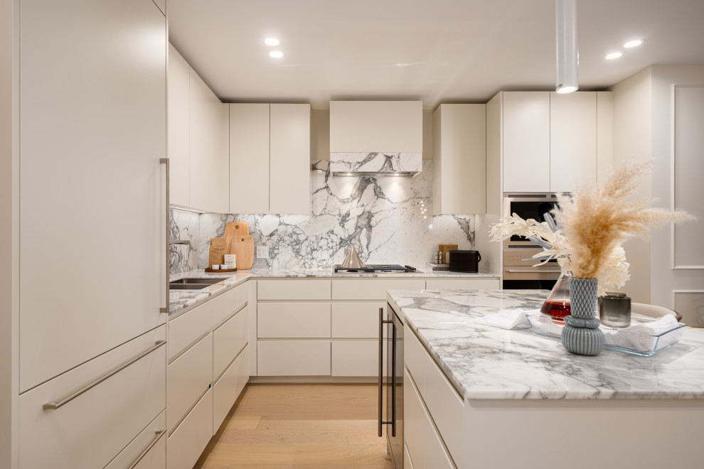 Example of a trendy l-shaped light wood floor and beige floor kitchen design with an undermount sink, flat-panel cabinets, white cabinets, stainless steel appliances, an island and white countertops
