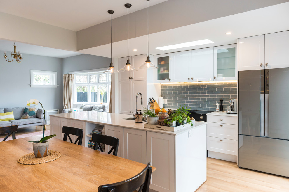 Inspiration for a mid-sized transitional galley kitchen in Christchurch with an undermount sink, shaker cabinets, white cabinets, quartz benchtops, subway tile splashback, stainless steel appliances, with island, blue splashback, light hardwood floors and brown floor.
