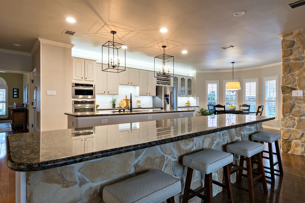 Inspiration for a large transitional galley medium tone wood floor open concept kitchen remodel in Dallas with an undermount sink, white cabinets, granite countertops, white backsplash, subway tile backsplash, stainless steel appliances and two islands