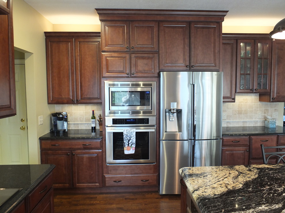 Inspiration for a large u-shaped medium tone wood floor eat-in kitchen remodel in Columbus with an undermount sink, raised-panel cabinets, brown cabinets, granite countertops, beige backsplash, ceramic backsplash, stainless steel appliances and an island