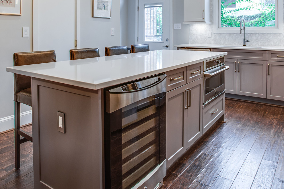 Eat-in kitchen - large transitional l-shaped medium tone wood floor and brown floor eat-in kitchen idea in DC Metro with an undermount sink, shaker cabinets, white cabinets, solid surface countertops, white backsplash, ceramic backsplash, stainless steel appliances, an island and white countertops