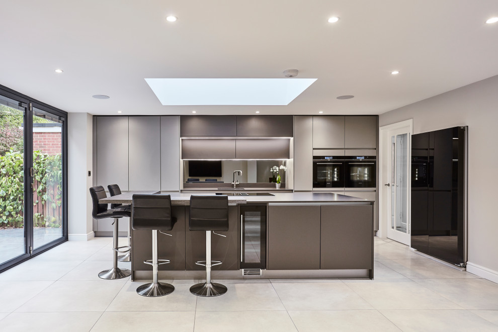 Design ideas for a mid-sized contemporary single-wall open plan kitchen in Other with flat-panel cabinets, grey cabinets, mirror splashback, black appliances, with island, an integrated sink, quartzite benchtops, metallic splashback, porcelain floors, grey floor, grey benchtop and vaulted.