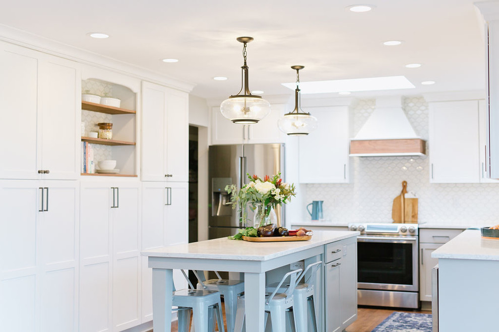 Example of a mid-sized transitional u-shaped medium tone wood floor and brown floor open concept kitchen design with an undermount sink, shaker cabinets, white cabinets, quartz countertops, white backsplash, porcelain backsplash, stainless steel appliances, an island and white countertops