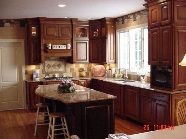 This is an example of a traditional eat-in kitchen in New York with raised-panel cabinets, medium wood cabinets, marble benchtops, yellow splashback, black appliances and medium hardwood floors.