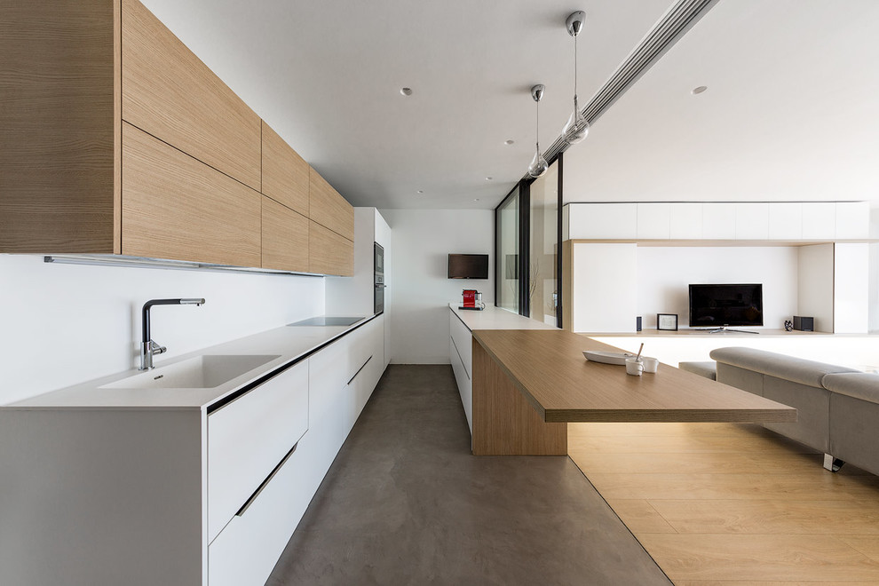 This is an example of a large contemporary open plan kitchen in Madrid with an integrated sink, flat-panel cabinets, light wood cabinets, white splashback, black appliances and a peninsula.