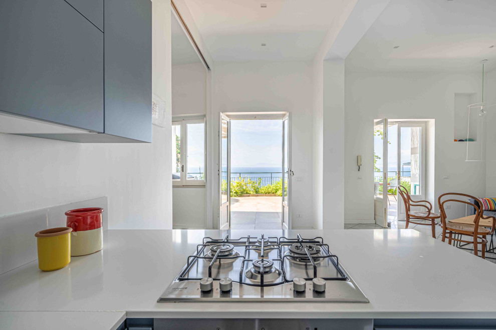 Photo of a mid-sized mediterranean u-shaped open plan kitchen in Naples with a drop-in sink, beaded inset cabinets, solid surface benchtops, white splashback, stainless steel appliances, ceramic floors, no island, white benchtop, recessed, turquoise cabinets, marble splashback and turquoise floor.