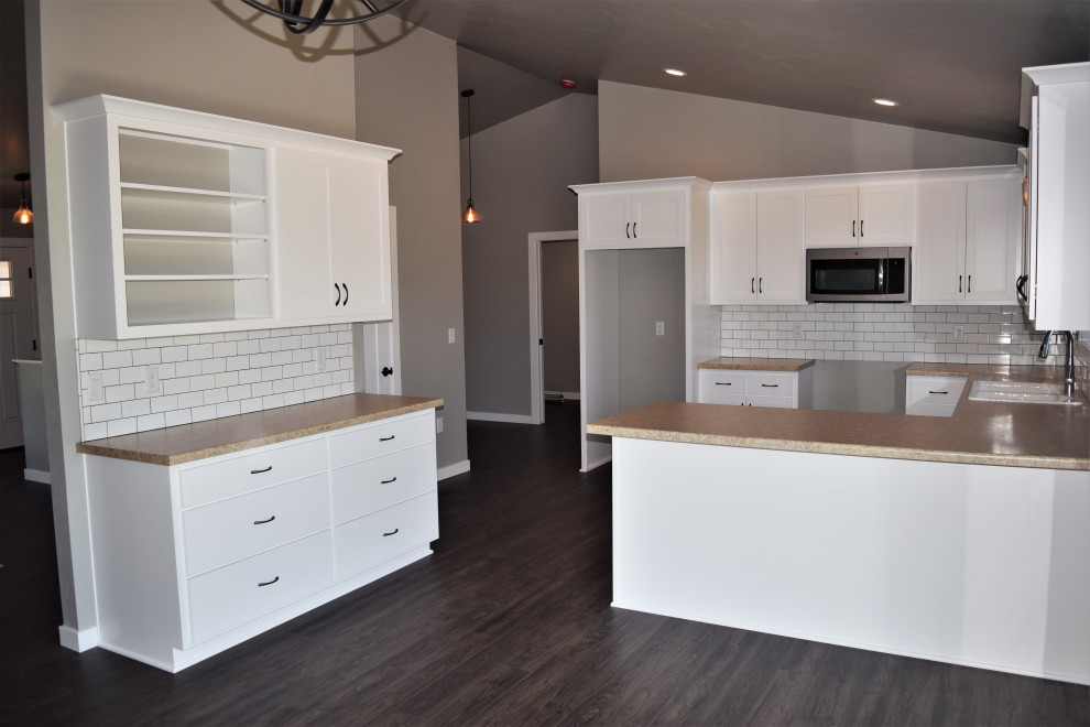 Large galley eat-in kitchen photo with a drop-in sink, recessed-panel cabinets, laminate countertops, ceramic backsplash, stainless steel appliances and a peninsula