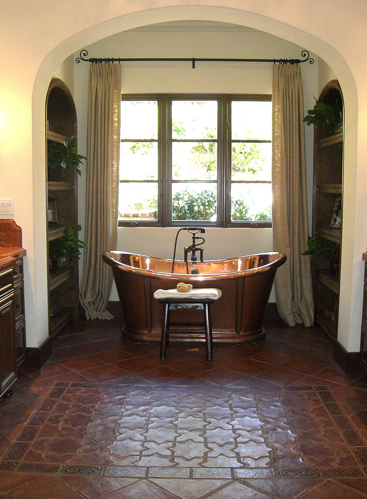 This is an example of an expansive mediterranean bathroom in Los Angeles with raised-panel cabinets, dark wood cabinets, a freestanding tub, a one-piece toilet, beige tile, brown tile, multi-coloured tile, red tile, porcelain tile, beige walls, porcelain floors, a drop-in sink, granite benchtops and red floor.