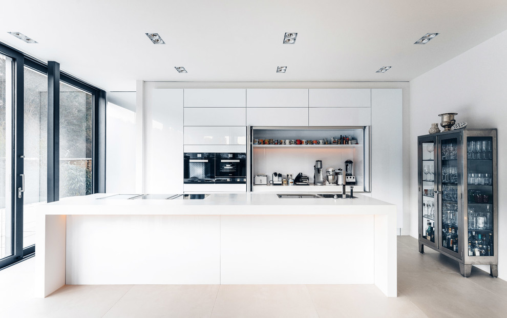 Inspiration for a large contemporary single-wall open plan kitchen in Cologne with a drop-in sink, black appliances, with island, flat-panel cabinets, white cabinets and limestone floors.