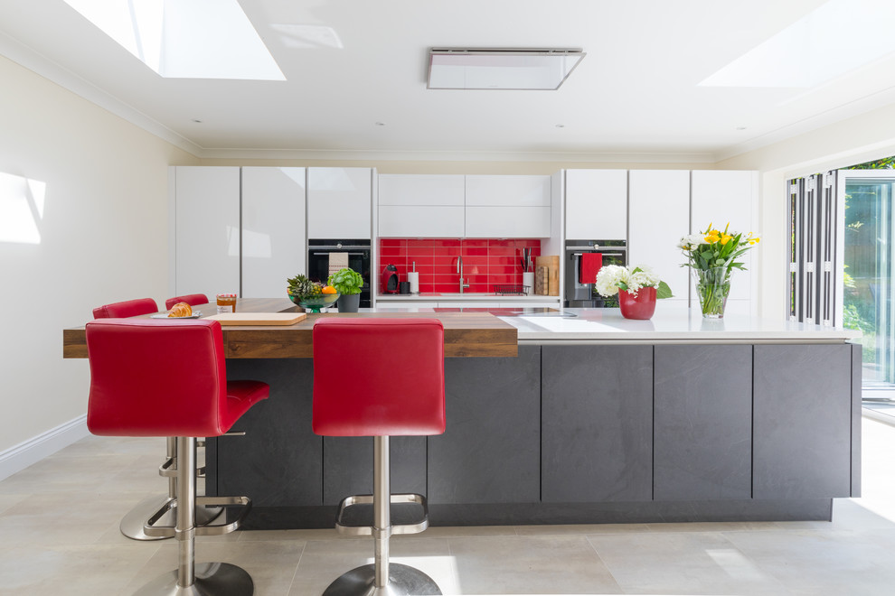 Photo of a mid-sized contemporary galley kitchen in Hampshire with an integrated sink, flat-panel cabinets, grey cabinets, quartzite benchtops, red splashback, porcelain splashback, panelled appliances, ceramic floors, with island, white benchtop and beige floor.