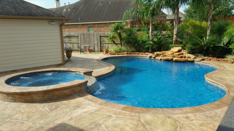 Inspiration for a mid-sized tropical backyard custom-shaped pool in Houston with a water feature and stamped concrete.