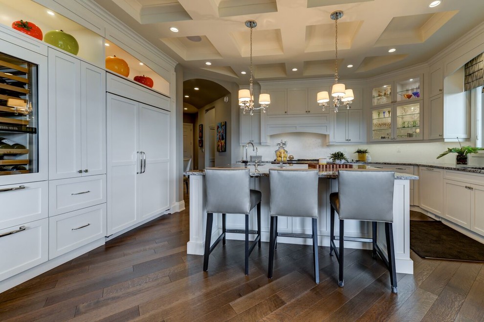 Large transitional u-shaped medium tone wood floor and brown floor kitchen photo in Edmonton with shaker cabinets, white cabinets, granite countertops, white backsplash, an island, an undermount sink, glass tile backsplash and paneled appliances