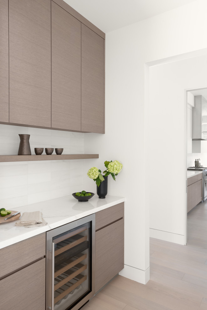 Modern kitchen in San Francisco with flat-panel cabinets, medium wood cabinets, marble benchtops, white splashback, marble splashback, panelled appliances, light hardwood floors, brown floor and white benchtop.